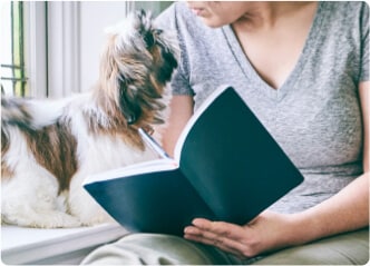 Woman taking educational course notes in a notebook while looking at her dog beside her.